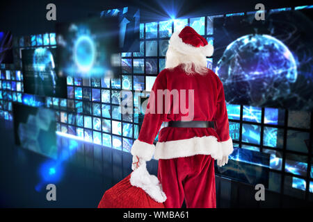 Santa carrying sack of gifts  against wall of digital screens in blue Stock Photo