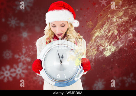 Happy festive blonde with clock against blurred christmas background Stock Photo