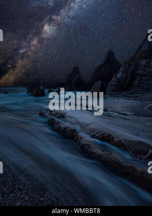 Beautiful composite landscape image of Mily Way core over sea rocks and cliffs with long exposure tide on beach Stock Photo