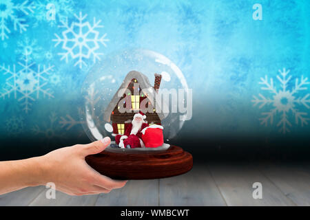 Composite image of hand holding snow globe against snowflake wallpaper over floor boards Stock Photo