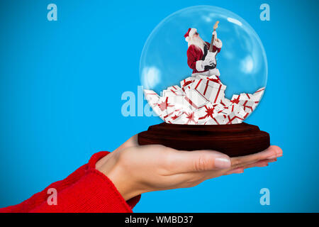 Composite image of hand holding santa snow globe against blue background with vignette Stock Photo