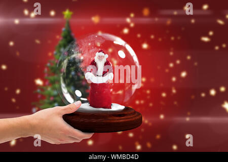 Composite image of hand holding snow globe against blurred christmas tree background Stock Photo