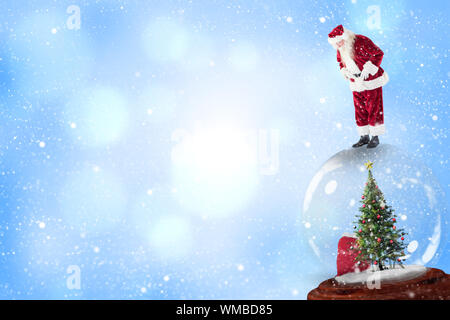 Santa standing on snow globe against blue abstract light spot design Stock Photo