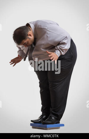 Obese man in formal clothes standing on a weighing machine shocked to see his weight Stock Photo