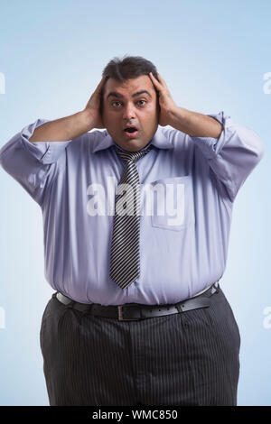 Obese man in formal clothes holding his head with both hands with an expression of shock Stock Photo