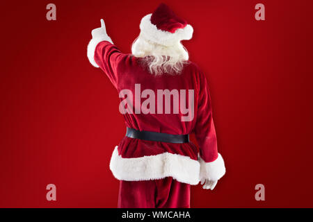 Santa Claus points at something against red background Stock Photo