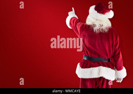 Santa Claus points at something against red background Stock Photo