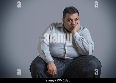 Obese man sitting in sad mood with chin resting on hand Stock Photo
