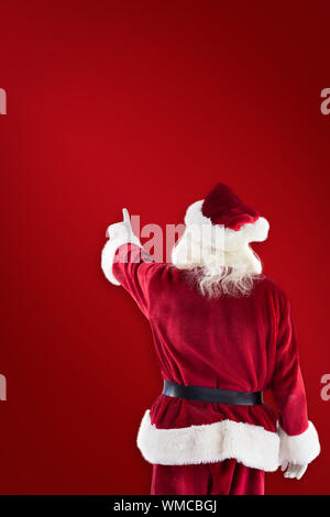 Santa Claus points at something against red background Stock Photo