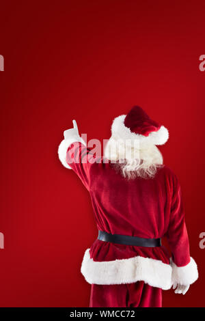 Santa Claus points at something against red background Stock Photo
