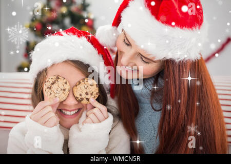 Festive mother and daughter on the couch with cookies against snow falling Stock Photo