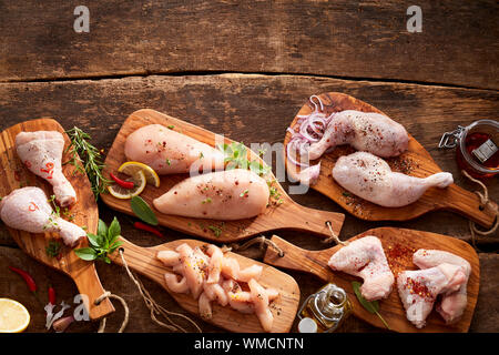 Assorted cuts and portions of raw chicken displayed on wooden boards with fresh herbs and spices in an overhead view on rustic wood with copy space Stock Photo
