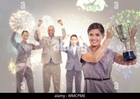 Woman holding up a cup with enthusiastic coworkers against colourful fireworks exploding on black background Stock Photo