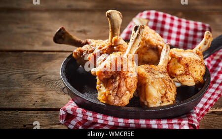 Pan or skillet filled with golden crispy fried spicy chicken portions on a rustic counter with checked red and white napkin Stock Photo