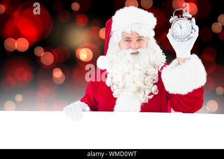 Santa claus holding alarm clock and sign against red glowing dots on black Stock Photo