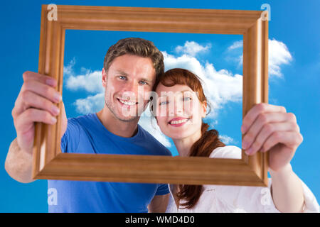 Couple holding frame ahead of them against cloudy sky Stock Photo