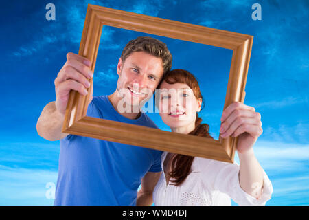 Couple holding frame ahead of them against blue sky Stock Photo