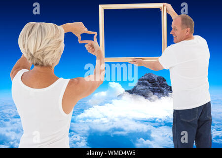 Mature couple hanging up picture frame against mountain peak through the clouds Stock Photo