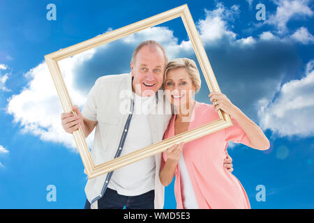 Older couple smiling at camera through picture frame against cloudy sky Stock Photo