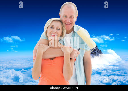 Happy older couple holding paint roller against mountain peak through clouds Stock Photo