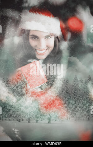 Festive brunette pressing gift at christmas against snowy landscape with fir trees Stock Photo
