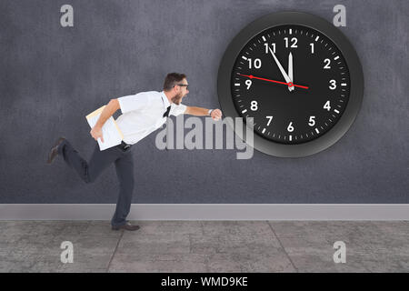 Geeky young businessman running late against grey room Stock Photo