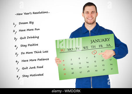 Smiling young mechanic in boiler suit pointing on bcalendar in his hands against green card Stock Photo
