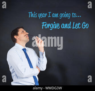 Thinking businessman biting glasses against blackboard Stock Photo