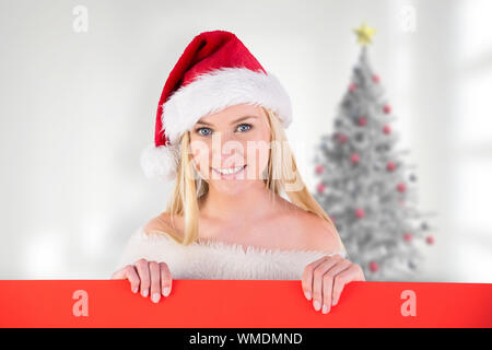 Festive cute blonde holding poster against blurry christmas tree in room Stock Photo