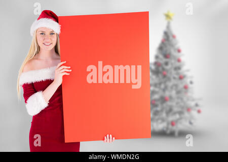 Festive cute blonde holding poster against blurry christmas tree in room Stock Photo