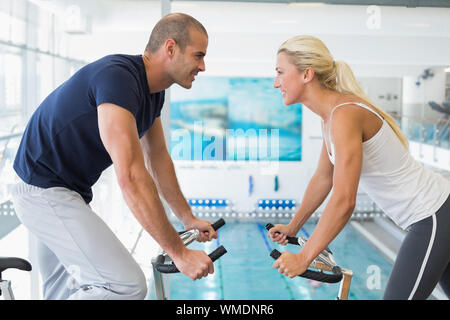 Side view of smiling fit couple working on exercise bikes at the gym Stock Photo