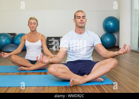 Sporty young couple sitting in lotus posture with eyes closed at fitness studio Stock Photo