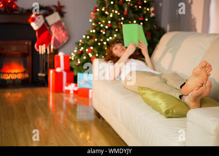 Relaxed redhead reading on the couch at christmas at home in the living room Stock Photo