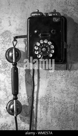 Vintage black phone hanging on old gray concrete wall. Black and white, retro style photo Stock Photo