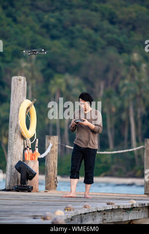 Asian man concentrate to controls and monitors drone on the sea jetty. Stock Photo
