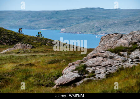 A man and a woman ride mountain bikes on a trail overlooking Loch Torridon on the Applecross Peninsula in the north west Highlands of Scotland. Stock Photo