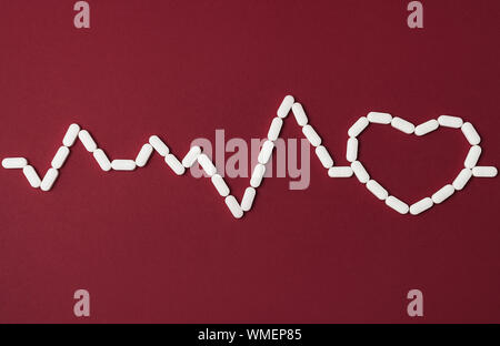 White pills in a shape of heartbeat and heart on red background. Flat lay style. Copy space. Medicine, healthcare and pharmacy concept. Stock Photo