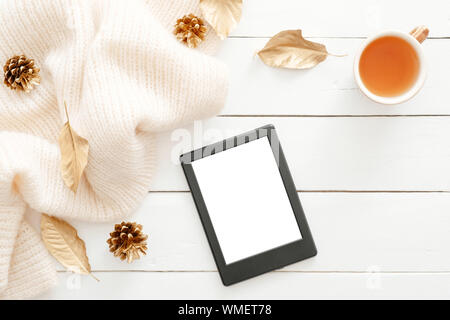 Autumn composition. Feminine desk table with knitted scarf, tea cup, cones, tablet ebook with blank screen, fall leaves on wooden background. Flat lay Stock Photo