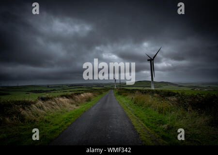 Wind Turbines along Hare Slack Hill above Ireleth in Cumbria.  Rakes Lane follows along the ridge line and cuts into the stormy landscape. Stock Photo