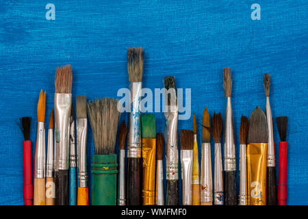 Set of dirty paint brushes on a blue painted canvas background Stock Photo