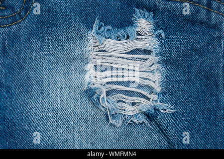 Hole and Threads on Denim Jeans. Close up blue jean texture Stock Photo