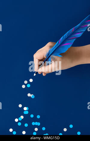 Christmas or New Year creative concept, hand drawing trail of paper snowflakes from blue feather quill on dark blue paper background Stock Photo