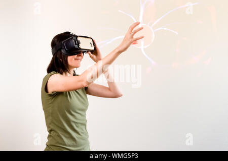 Caucasian woman with brown hair in green t-shirt wearing virtual reality goggles on white background. Future technology concept. Stock Photo