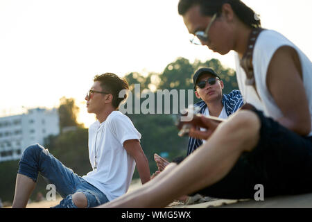 young asian adult men sitting on beach relaxing and playing guitar Stock Photo
