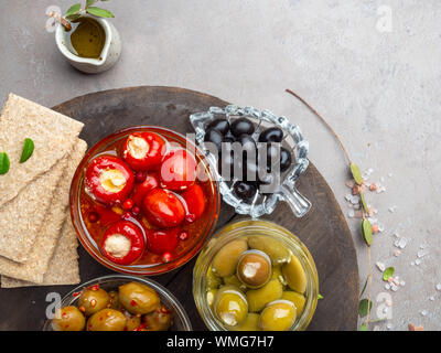 Italian food ingredients background with crackers, olive oil, mini bell peppers stuffed with cheese, olives and herbs on gray stone slate Stock Photo