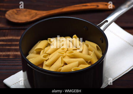 Cooked noodles (Penne Rigate) inside an professional anodized nonstick aluminum pan over a napkin on a vintage wooden surface Stock Photo