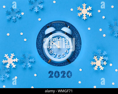 Happy New Year 2020! Aarm clock in paper hole with torn space for your text, flat lay on blue paper background Stock Photo