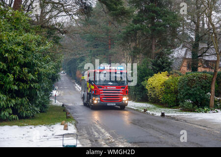 A red Scania P270 fire engine with flashing lights attends an emergency on a cold snowy morning in winter, Woking, Surrey, southeast England Stock Photo