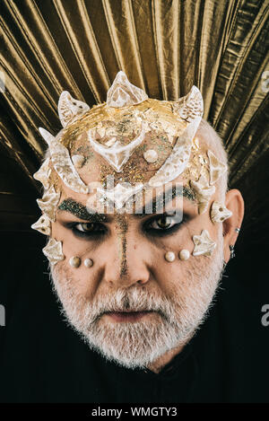 Demon head wearing golden collar appearing from darkness, nightmare concept. Evil monster with glittering skin and thorns on face on black background Stock Photo