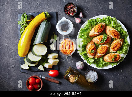 Toasted bruschetta with vegetable Mash, Puree, caviar cooked of zucchini, tomato, carrot and spices served on a white plate. ingredients on a concrete Stock Photo